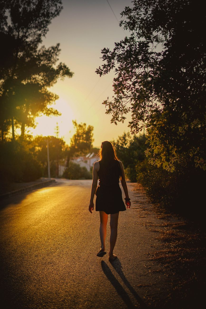 back view of a woman in black dress walking on the concrete road during sunset