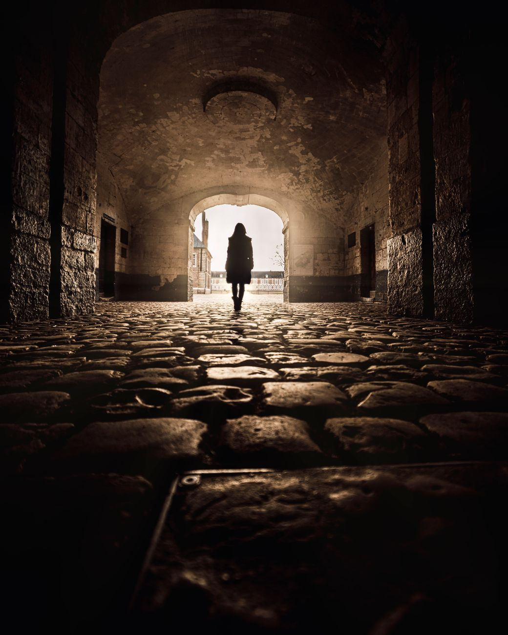 silhouette of woman walking through gate on cobblestone pavement